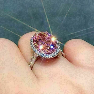 Elegant oval pink zircon ring with halo crystals and shimmering silver band on finger