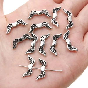 Detailed antique silver wing charms with heart centers held in hand for scale reference
