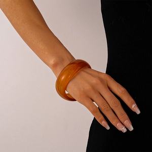 Macro detail of amber resin bangle with marble texture on a model wearing black clothing