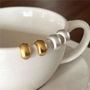 Minimalist U-shaped frosted gold and silver earrings on a white ceramic cup edge