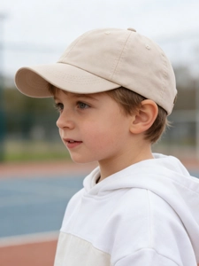 Side view of a boy wearing a beige cotton baseball cap in an outdoor sports setting