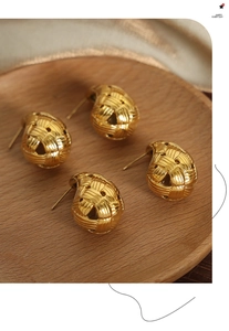 Detailed view of woven hollow ball earrings in gold stainless steel on wooden tray