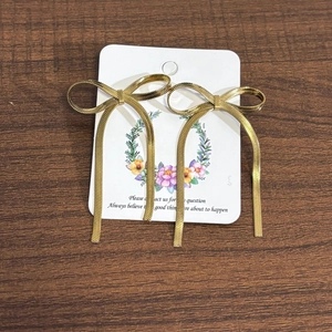 Close-up of 18K gold stainless steel bow earrings with mesh chain tassels on a card