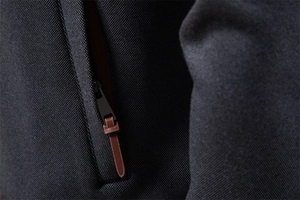 Macro detail of dark grey textured fabric with a black zipper and brown pull tab
