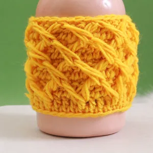 Detail of yellow handmade crochet mug sleeve with 3D cable knit texture on a pink bottle