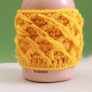 Detail of yellow handmade crochet mug sleeve with 3D cable knit texture on a pink bottle