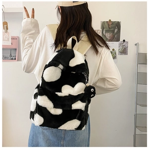 Detail of plush black and white cow print backpack with decorative fuzzy coal sprite charm