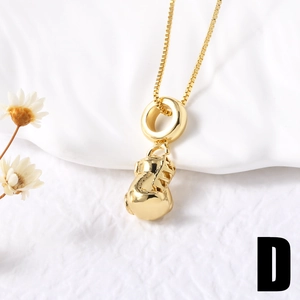 Detail of a polished gold boxing glove pendant necklace on a minimalist fabric background