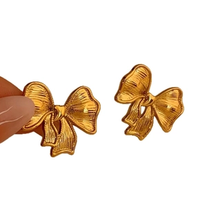 Polished gold bow earrings with brushed metal texture shown in a hand-held close-up