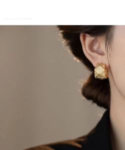 Close-up of gold chunky C-shaped hoop earrings with irregular hammered texture on model