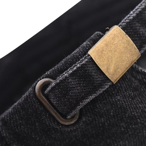 Vue détaillée macro du denim noir lavé avec boucle en laiton vintage et œillets métalliques