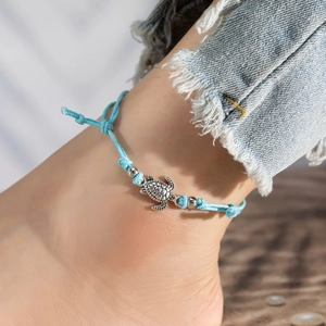 Close-up of light blue braided turtle anklet with silver beads on woman's ankle
