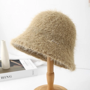 Détail du chapeau bob en fourrure beige avec badge métallique sur support en bois