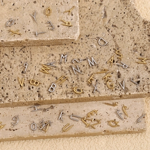 Flat lay of 18K gold and silver letter pendants on natural stone texture background
