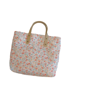 Floral canvas tote bag with orange patterns and brown leather handles on white background