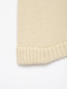 Close-up of beige knit fabric texture showing fine stitch patterns and ribbed hem detail