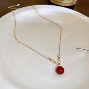 Makro-Detail einer vergoldeten Halskette mit roter Perle und goldenen Akzentperlen