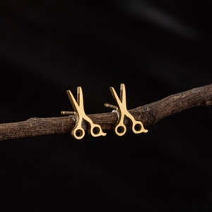 Minimalist gold scissors stud earrings displayed on a rustic branch background