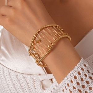 Détail du large bracelet jonc doré avec design tissé en cage et petites perles d'or