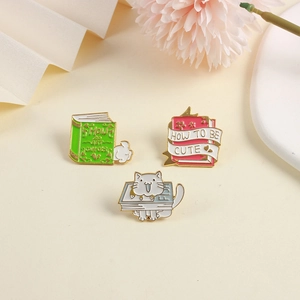 Detail of three enamel cat and book brooches with How to be Cute and Fish text