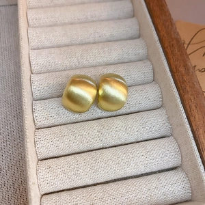 Detailed view of matte brushed gold curved earrings in a luxury wooden jewelry box
