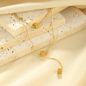 Detail of gold cube pendants on a snake chain over beige fabric and stone backdrop