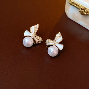 Detailed close-up of bow earrings with white enamel finish and hanging round pearls