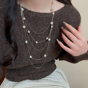 Close-up of a layered golden necklace with white pearls over a brown sweater