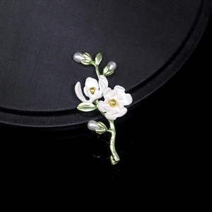 Detail of white enamel flower brooch with green leaves and teardrop pearls
