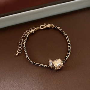Detail of gold floral cylinder pendant and crystal ring charm on a black woven chain necklace