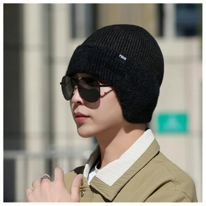 Détail d'un bonnet en tricot noir avec protège-oreilles et logo FBKS sur un modèle