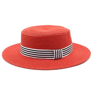 Detail of red boater straw hat featuring a chic black and white striped ribbon band