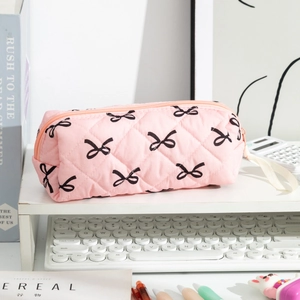 Pink quilted pencil case with bow patterns and carry strap shown in a desk setting