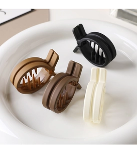 Four matte hair claw clips in earth tones arranged on a white ceramic plate for styling