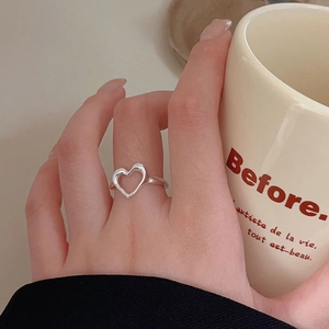 Detail of a minimalist 925 silver hollow heart ring worn on finger holding a mug