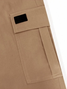 Detail of khaki twill cotton cargo pants showing a side pocket and black decorative patch