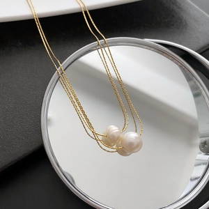Elegant gold titanium necklace with three white pearls shown in a creative mirror reflection