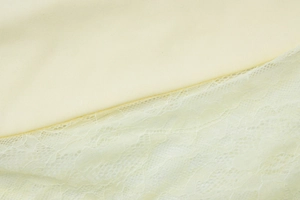 Macro shot of light yellow plain fabric with delicate lace patchwork on a summer dress