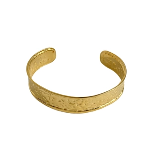 Golden stainless steel cuff bracelet with irregular hammered texture on white background