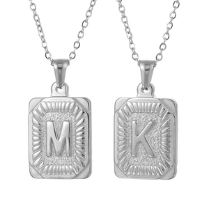 Macro shot of silver rectangular pendants with engraved letters M and K on metal chains