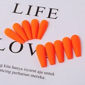 Detail of matte bright orange press-on nails in long coffin shape on a white background