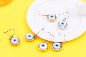 Detail of gold and silver evil eye dangle earrings with blue charms on yellow background