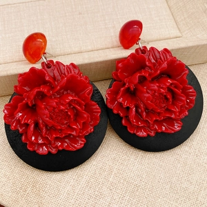 Détail de boucles d'oreilles fleurs 3D rouges avec base noire sur présentoir en lin