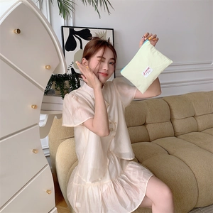 Model holding a small yellow macaron makeup bag with a blue zipper in a cozy room