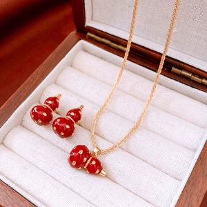 Detailed close-up of 18k gold plated red gourd pendant necklace and earrings set in jewelry box