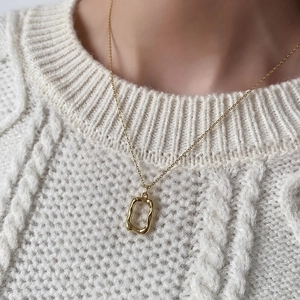 Close-up of golden irregular textured necklace worn on a cream cable-knit sweater