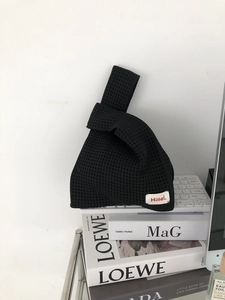 Detail of black waffle knit handbag with red label on a minimalist indoor desk