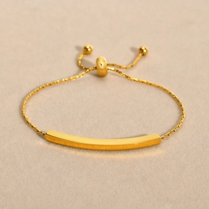 Minimalist gold stainless steel bar bracelet with adjustable sliding clasp on beige fabric