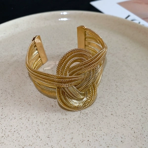 Detail of golden metal braided open bangle with a large twisted knot design and smooth finish