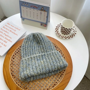 Detail of chunky knit mixed blue and green beanie with rolled edge on a wooden tray